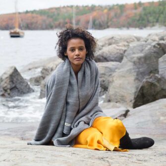 Swans Island's Acadia Throws are woven in Maine with organic Merino wool and organic American Cotton. Organic Washable Wool, extra soft. Hand-dyed colors. Shown here in Graphite. Model wrapped in Acadia throw by the water.