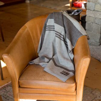 Swans Island Company - Island Throw - 100% wool from Maine island sheep. Handwoven in Grey with Brown. Shown here on a leather chair at the Vinalhaven,Maine farm where the fleece for these throws came from.