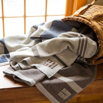Swans Island Company's Island Throw captures the essence of the Maine. Woven by hand in our Maine studio with locally sourced island wool. Shown here in three colorways of grey with brown, and blue.stripes