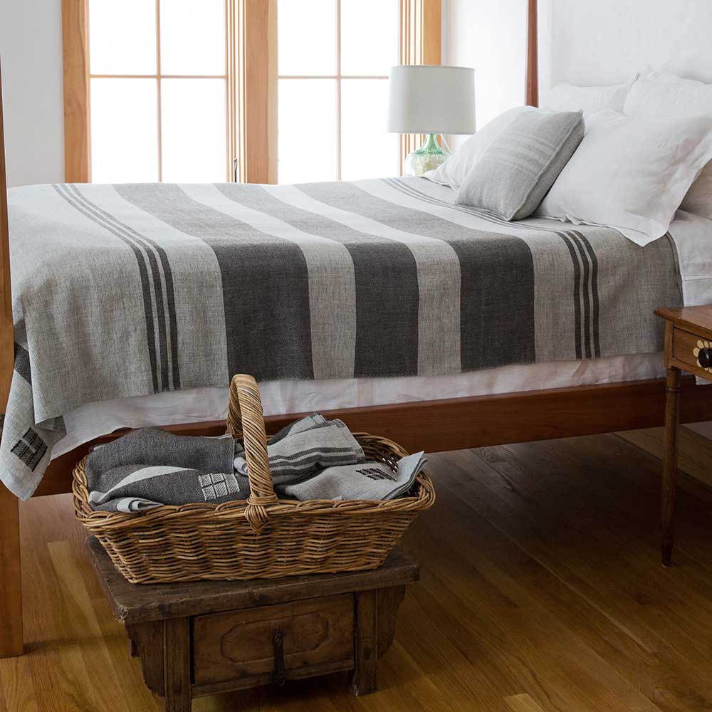 Swans Island Company's Island Blankets are handwoven in Maine with single-source wool from one Maine island farm. Shown here Grey blanket with brown stripes on a bed.