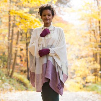 Swans Island Company's Maine Coast Cape. Handwoven in Maine with soft organic merino wool and touch of alpaca. Colors are dyed with all natural dyes. Shown here in Beetroot on woman walking with yellow fall foliage in the background.