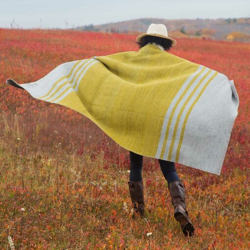 Woman in red autumn field with a Swans-Island Mt. Kineo-Throw shown here in Granite + Lichen, hand-dyed and handwoven in Maine.