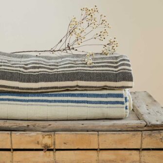 A stack of Swans Island handwoven Grace Winter Blankets. Shown here in Charcoal + Natural and Natural + Indigo.