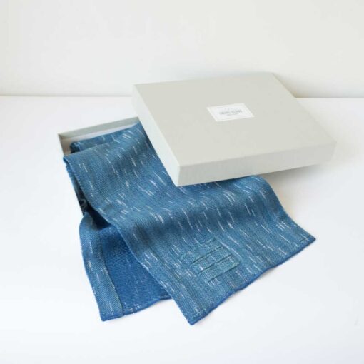Swans Island Company's Firefly Scarf is handwoven in Maine with uniquely hand-dyed yarn. Soft organic merino wool has flecks of white reminiscent of fireflies twinkling against a night sky. Shown here in Blue Spruce in our signature linen gift box.