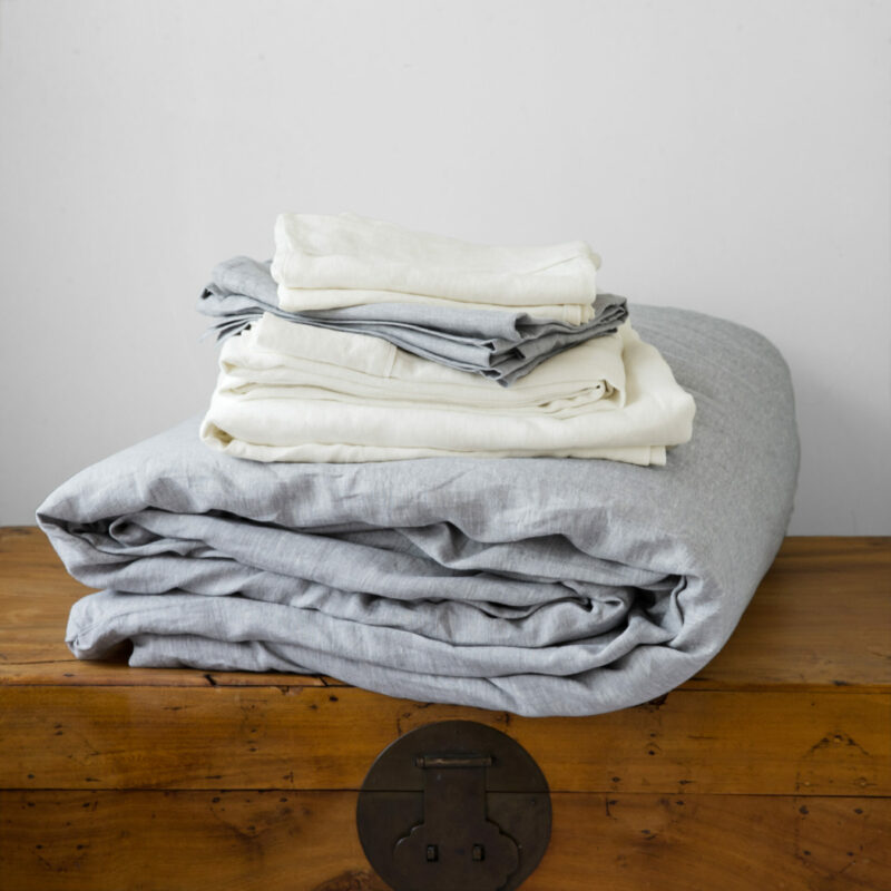 A stack of Swans Island's Classic linen sheet set in ivory and and Chambray linen duvet set in Pewter Grey.