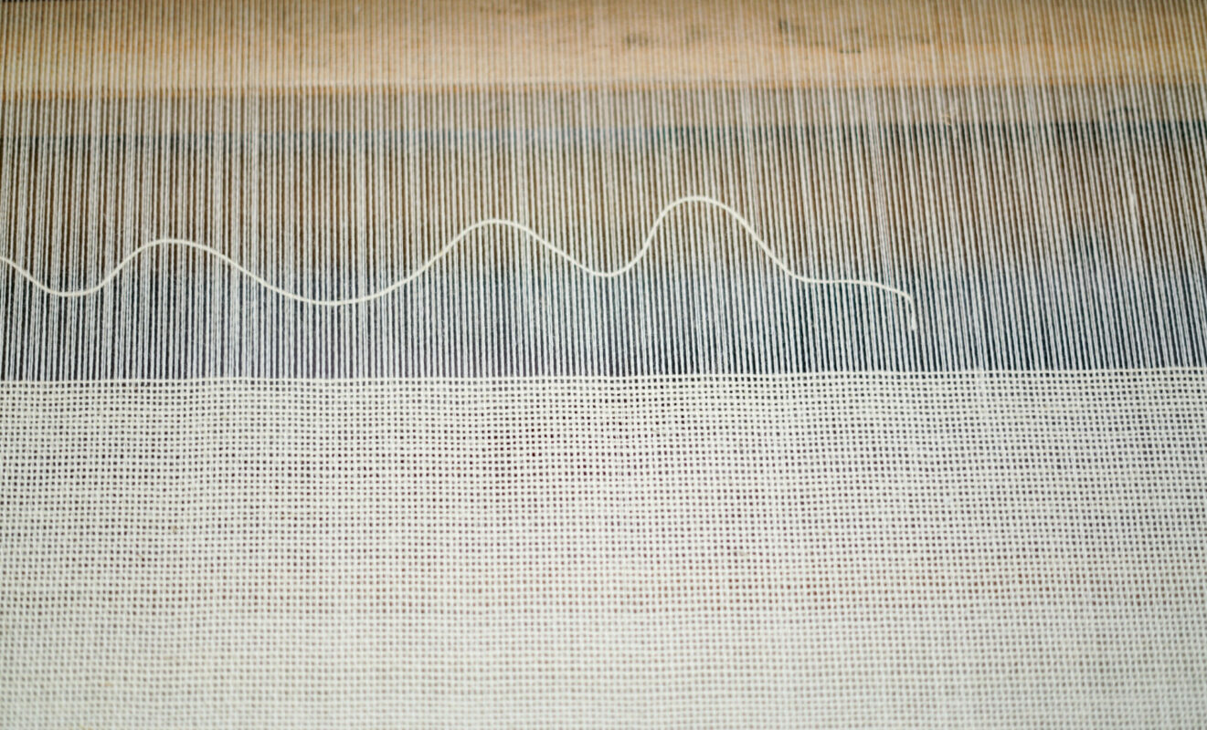 A single weft yarn wavers above a ground of plain weave creating a modern a graphic design on the loom at Swans Island Company.