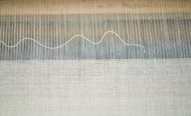 A single weft yarn wavers above a ground of plain weave creating a modern a graphic design on the loom at Swans Island Company.