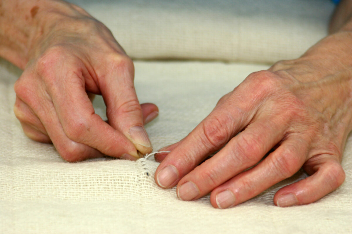 A seamstresses hands in the Swans Island finishing room, repairing a broken thread in a handwoven blanket.