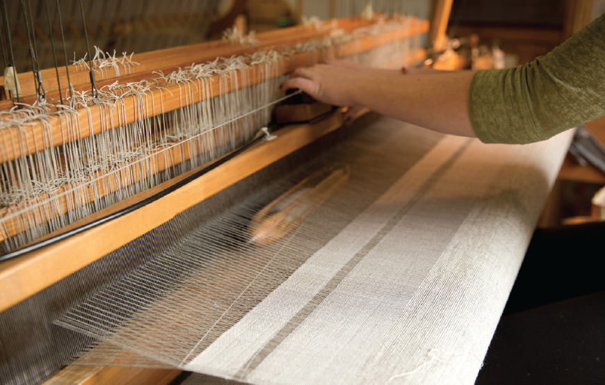 A weavers hands at the loom as the shuttle filled with yarn travels across the loom at the Swans Island handweaving studio in Northport, Maine.