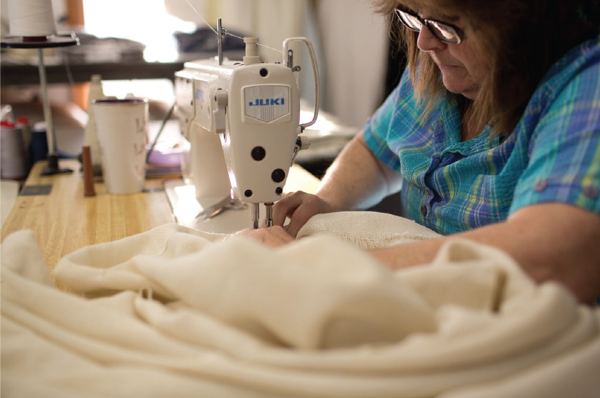 In the finishing room at Swans Island, Louise stitches the silk binding at the edge of a handwoven blanket.
