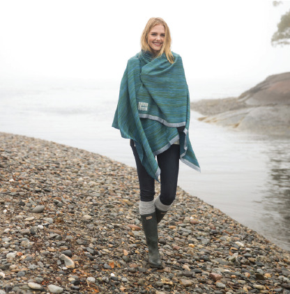 Model is wrapped in Swans Island's handwoven Watercolors Throw in indigo and teal on a foggy day at the Maine shore.