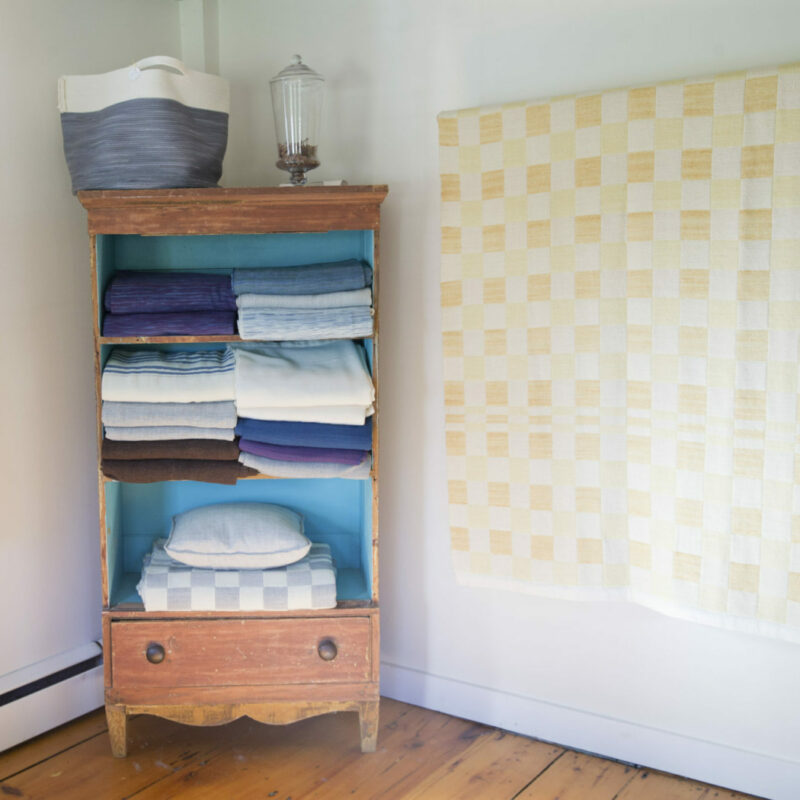 Handwoven blankets fill a vintage armoire at the Northport, Maine farmhouse of Swans Island Company.