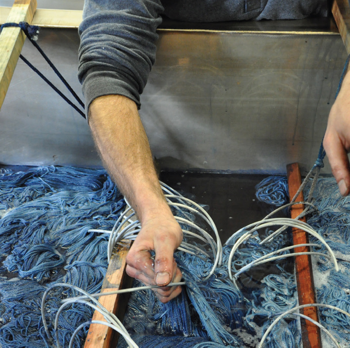 The skilled hands of the master dyer at Swans Island Co. move skeins of yarn in an indigo dye bath.