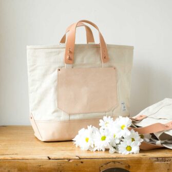 Swans Island Company's Canvas Bucket Tote in heavy cotton canvas with leather bottom and pocket, removable leather handles, and cotton webbing shoulder straps - by Immodest Cotton. Natural