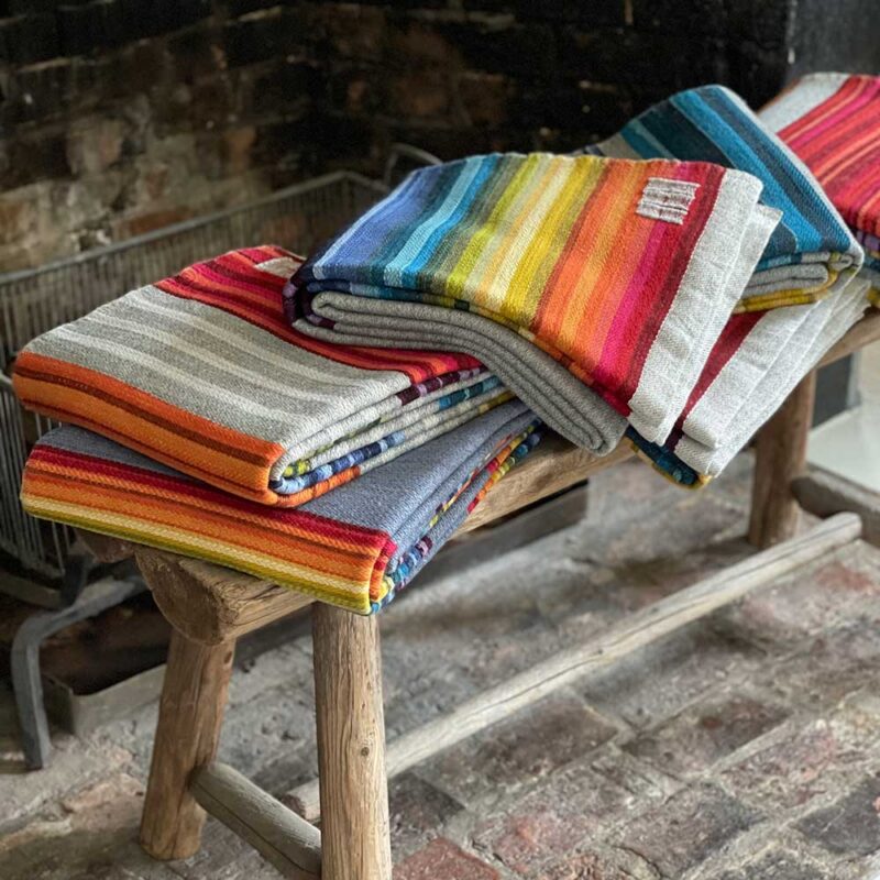 Swans Island Company's Limited Edition Prism Series Throws. Nine rainbow-inspired throws designed by our team of talented weavers. Each throw in this limited edition drop is unique! A stack of beautiful finished Prism Throws await their new homes.