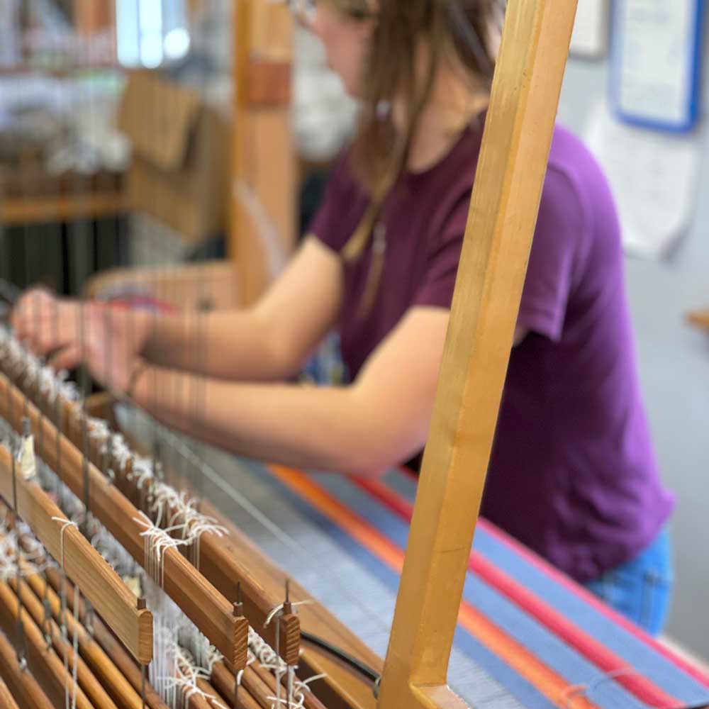 Swans Island Company's Limited Edition Prism Series. Nine rainbow-inspired throws designed by our team of talented weavers. Each throw in this limited edition drop is unique! Here's Chloe working at the loom making one of the nine unique throws.