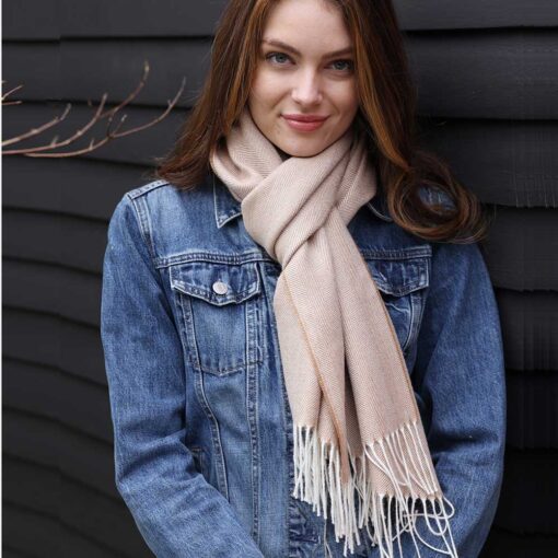 Swans Island Company's Baby Alpaca Scarf is woven in Peru with the softest baby alpaca. Lightweight and generously proportioned, this scarf has a classic herringbone twill pattern with fringed edges. . Shown here in Camel with natural, on a female model wearing a jean jacket.
