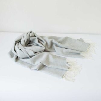 Swans Island Company's Baby Alpaca Scarf is woven in Peru with the softest baby alpaca. Lightweight and generously proportioned, this scarf has a classic herringbone twill pattern with fringed edges. . Shown here in Light Grey with natural.