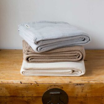 Swans-Island Company's Cashmere Mini-Cable Blankets are woven in Maine with a soft blend of 70% American cotton + 30% Cashmere Shown here in Frost, Hazlenut and Muslin.