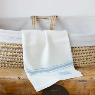 Swans Island Company's classic Grace Baby Blankets. Handwoven in Maine with soft organic merino wool yarns. Pure undyed organic merino wool with an assortment of rich hand-dyed stripe colors. Each blanket comes in a beautiful presentation gift box, perfect for gifting. Shown here in White with Sky Blue stripes.