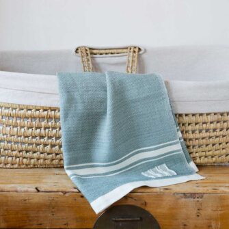 Swans Island Company's Modern Grace Baby Blankets. Handwoven in Maine with soft organic merino wool yarns in an assortment of rich hand-dyed colors. Each blanket comes in a beautiful presentation gift box, perfect for gifting. Shown here in Sage with natural stripes.
