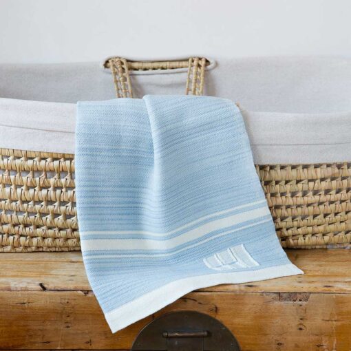 Swans Island Company's Modern Grace Baby Blankets. Handwoven in Maine with soft organic merino wool yarns in an assortment of rich hand-dyed colors. Each blanket comes in a beautiful presentation gift box, perfect for gifting. Shown here in Sky Blue with natural stripes.
